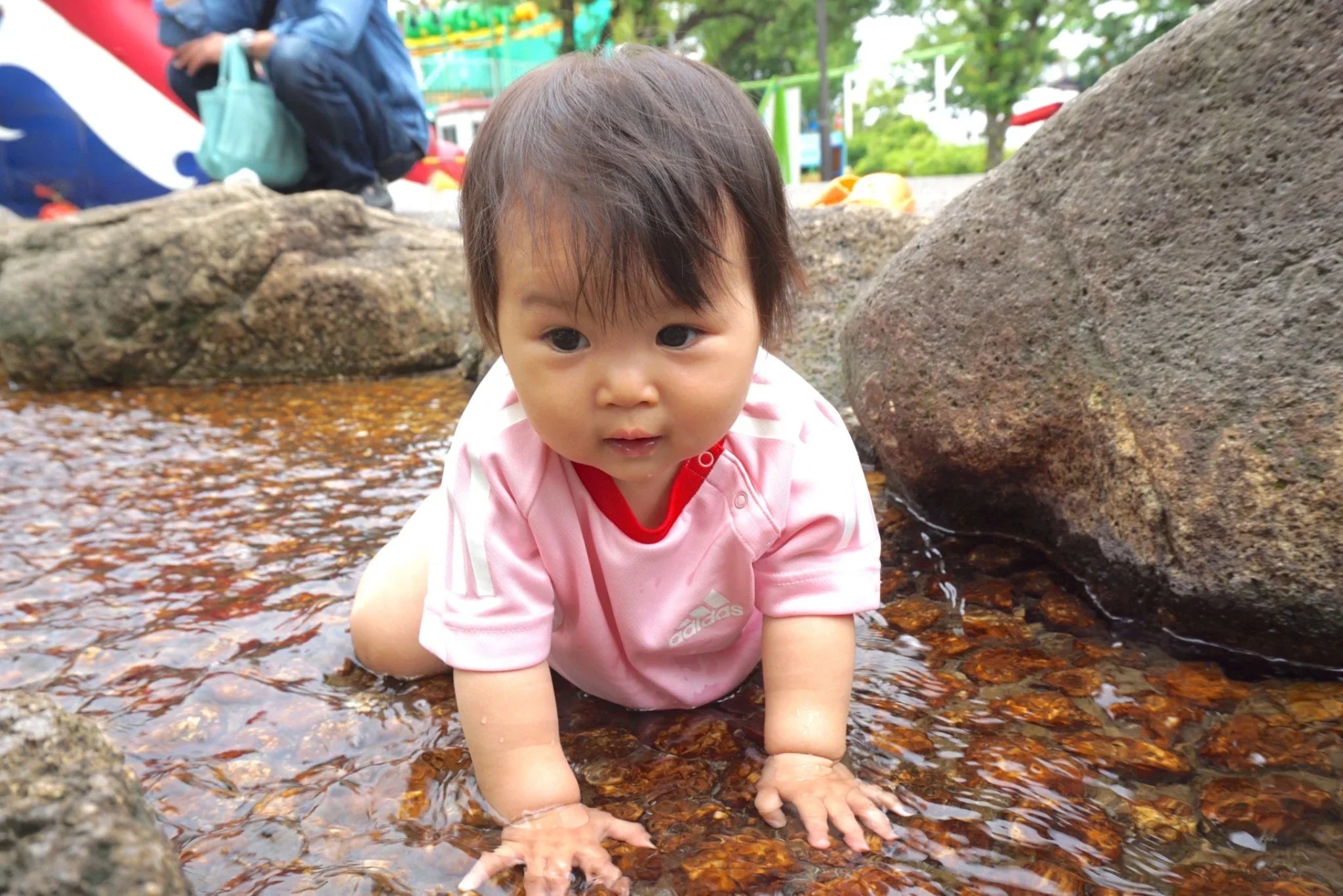 A baby playing in a shallow stream, representing natural clean water and safe hydration for families.