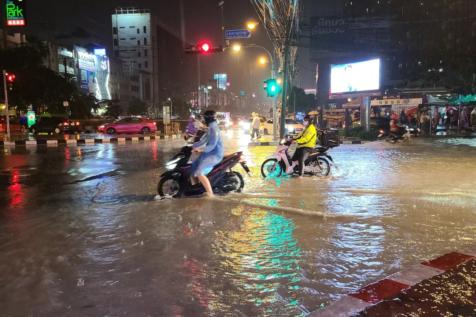 Bangkok flooded intersection at night during heavy rain with motorcycles and traffic