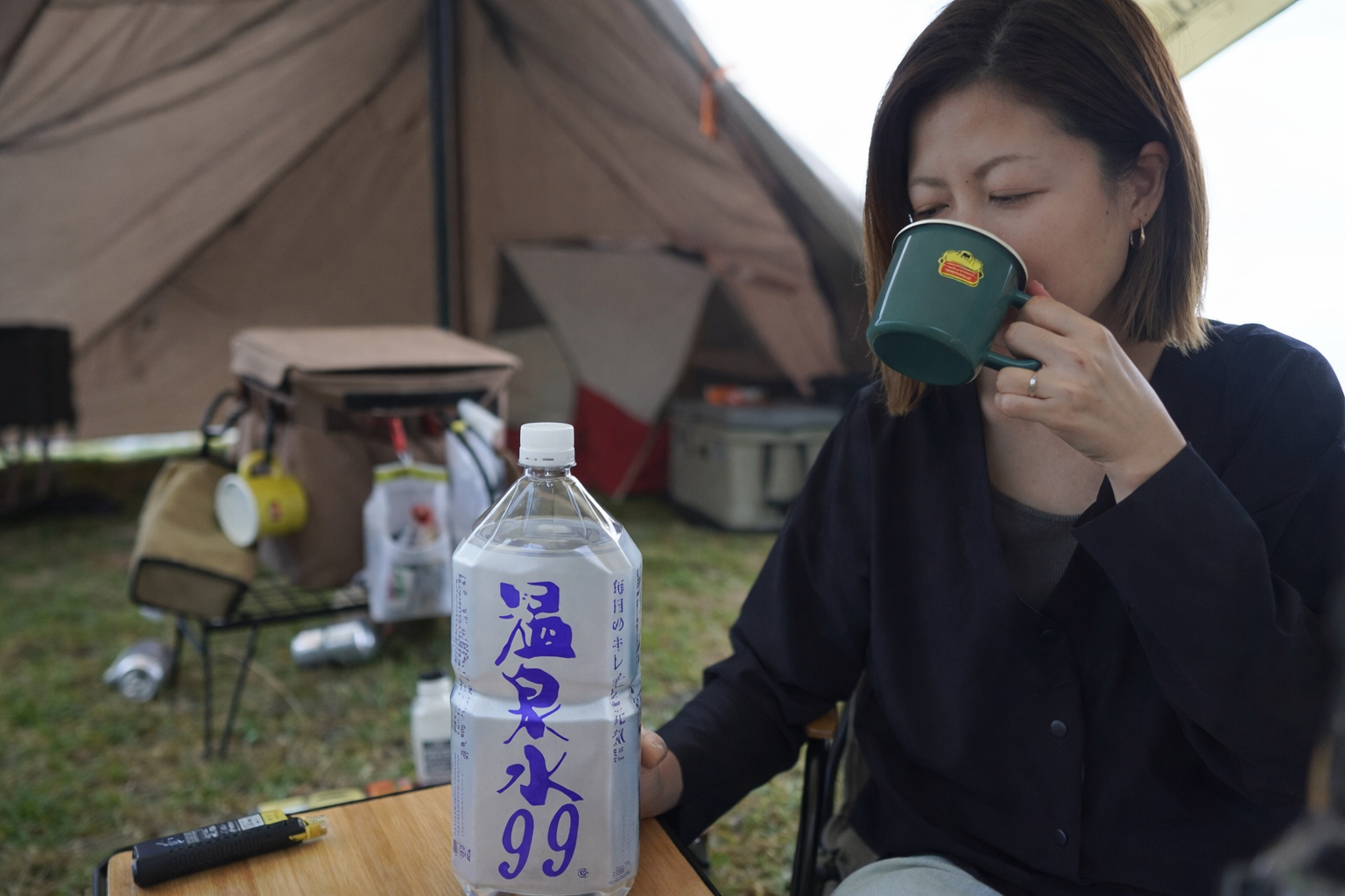 キャンプで自然を楽しみながら温泉水99を飲む女性