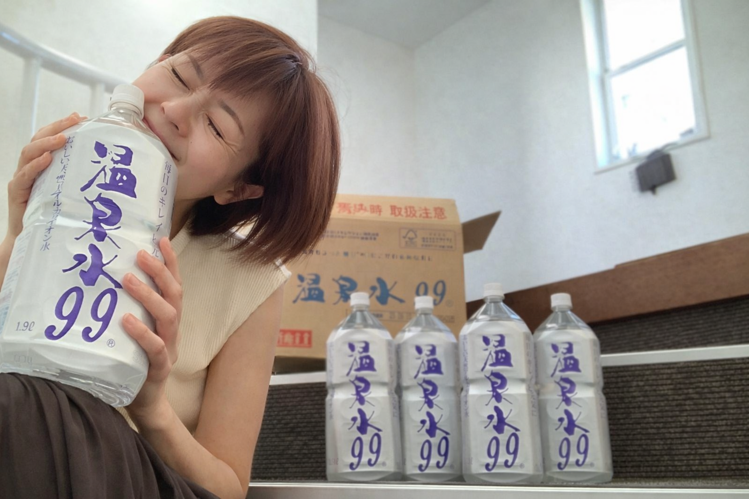 階段に並べられた温泉水99のボトルを抱きしめ、喜ぶ女性