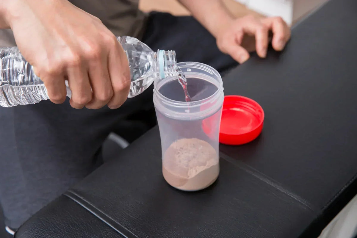 Water being poured into a protein shaker, illustrating how water type affects protein mixing and drinkability.