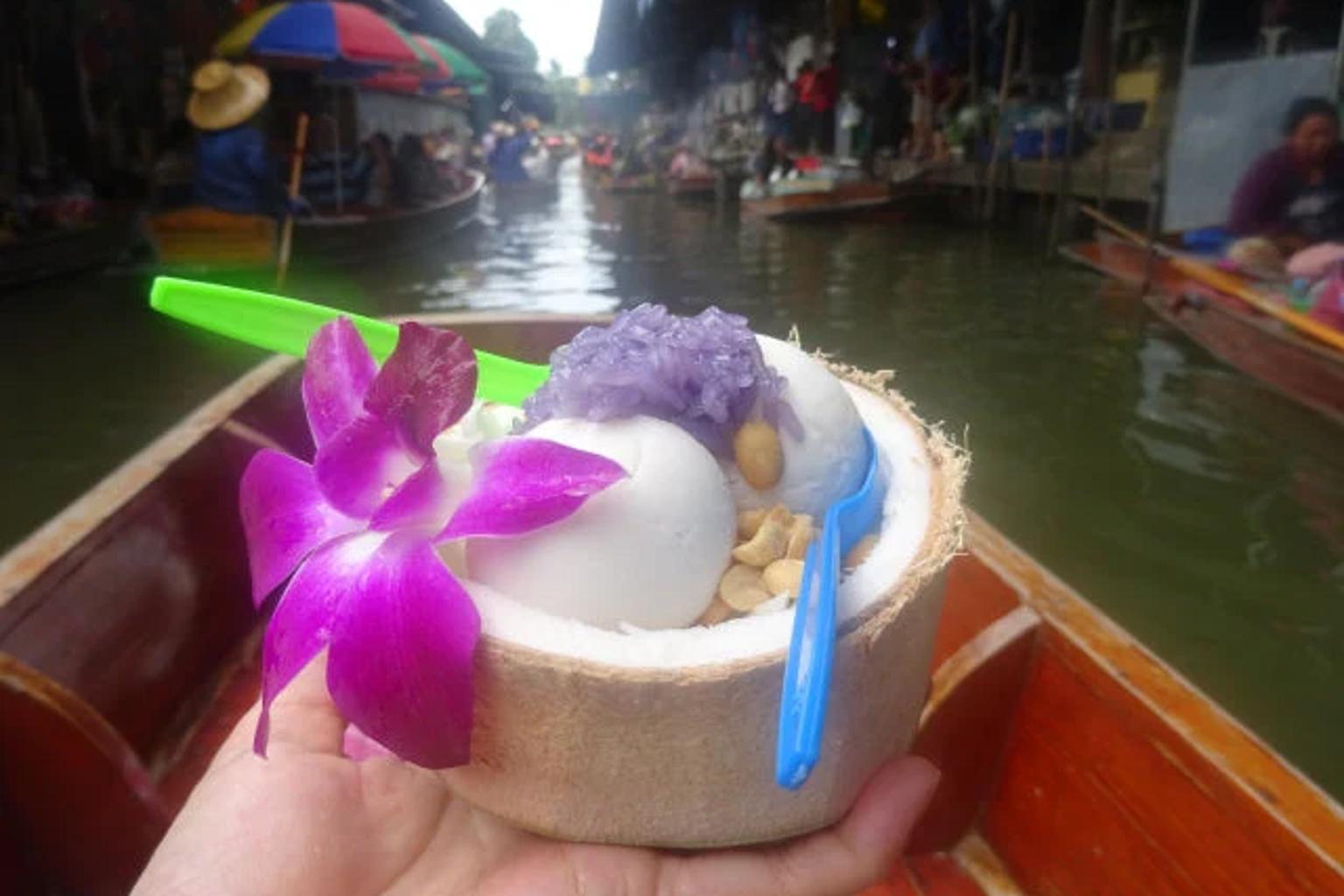 タイの水上マーケットで販売されるココナッツアイスクリーム。花ともち米が添えられたトロピカルスイーツ
