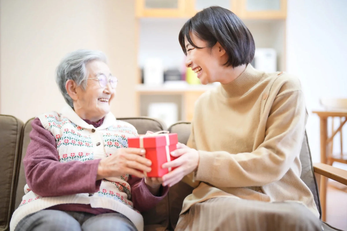 A Japanese woman giving a heartfelt gift to her grandmother, representing gratitude and thoughtful giving with ONSENSUI99 from Japan.