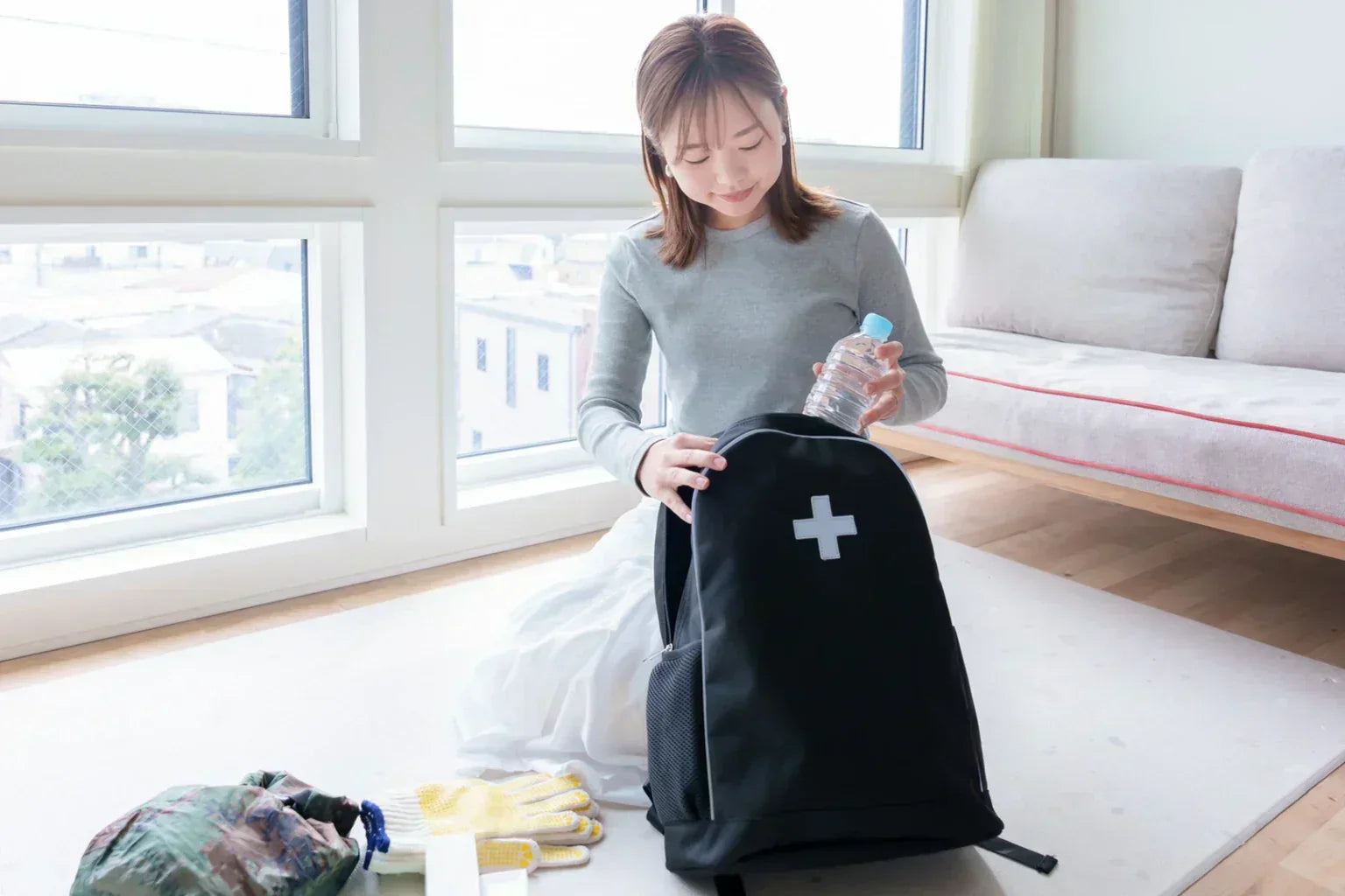 Woman preparing emergency backpack with bottled water at home