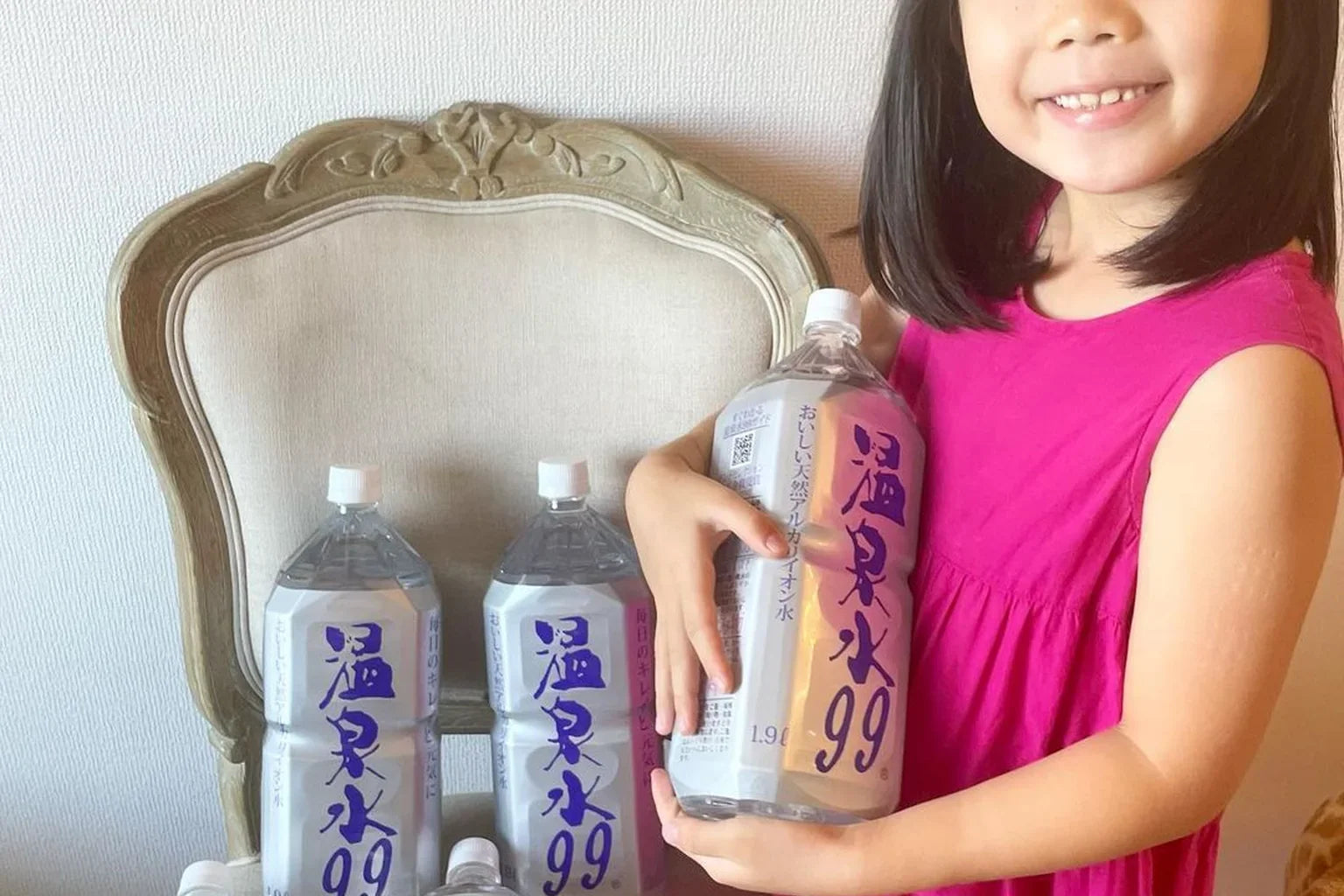 Smiling girl holding ONSENSUI99 water bottle at home with family stock of natural drinking water for kids