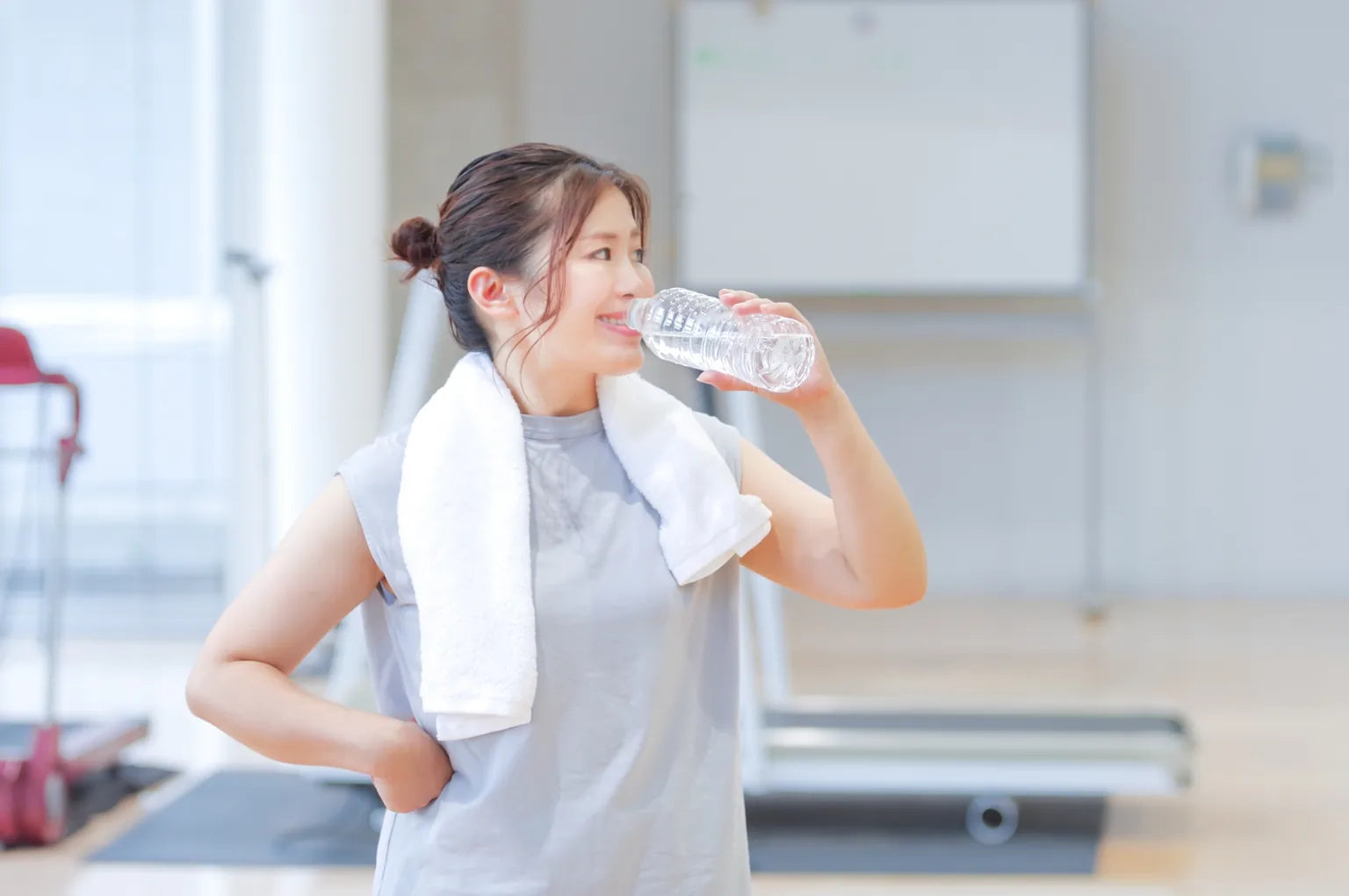 Japanese woman drinking water after a workout, showing clean hydration and the refreshing image of ONSENSUI99 soft water.