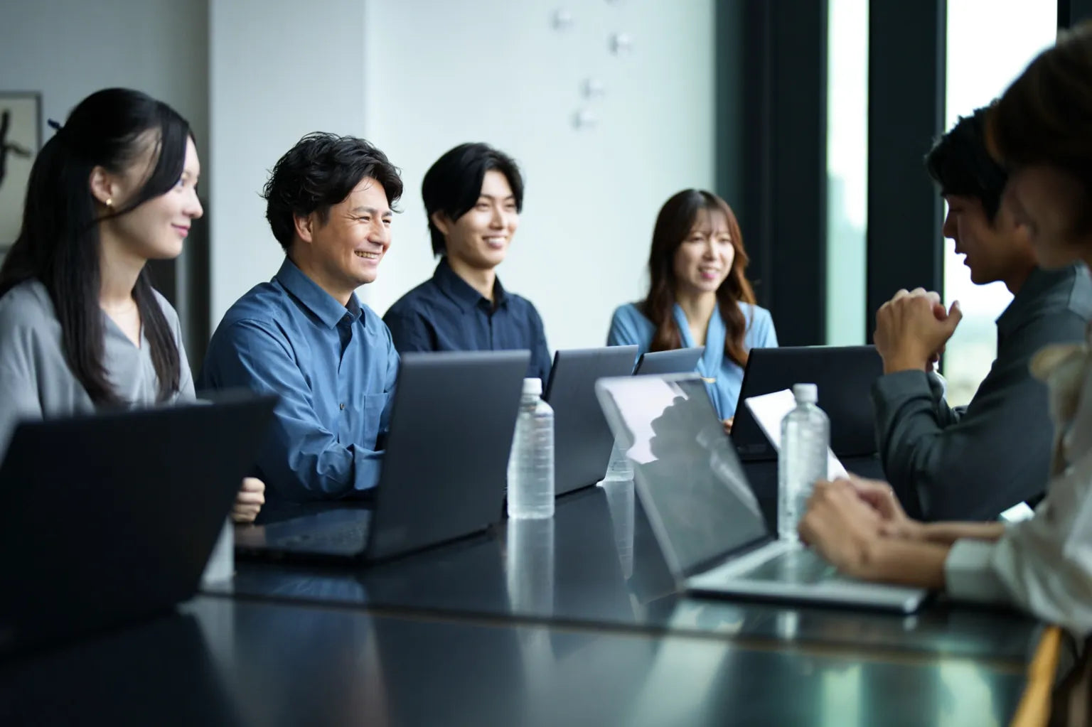 Japanese business team in a meeting with laptops and water bottles, showing healthy hydration with soft water in the workplace.