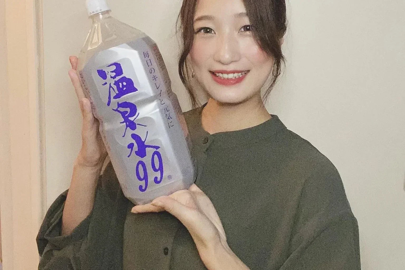 Japanese woman smiling while holding ONSENSUI99 bottle, representing premium Japanese soft water lifestyle.