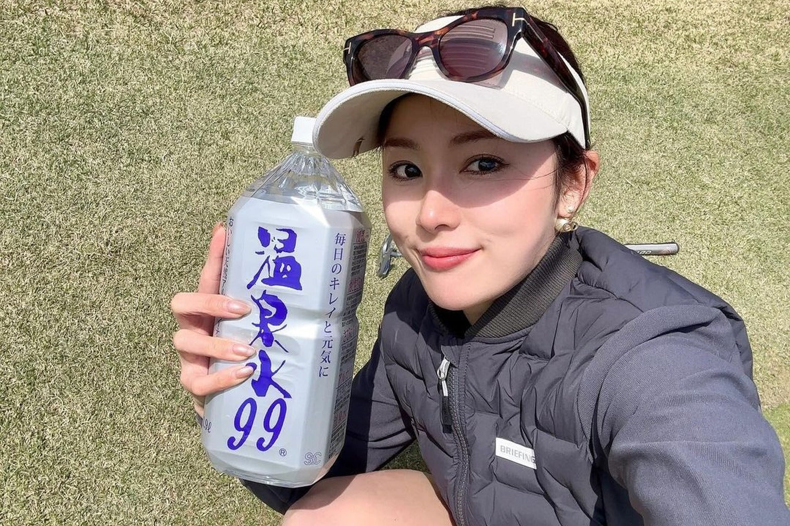 ゴルフ場で水を飲む日本人女性。スポーツ後の水分補給をイメージ
