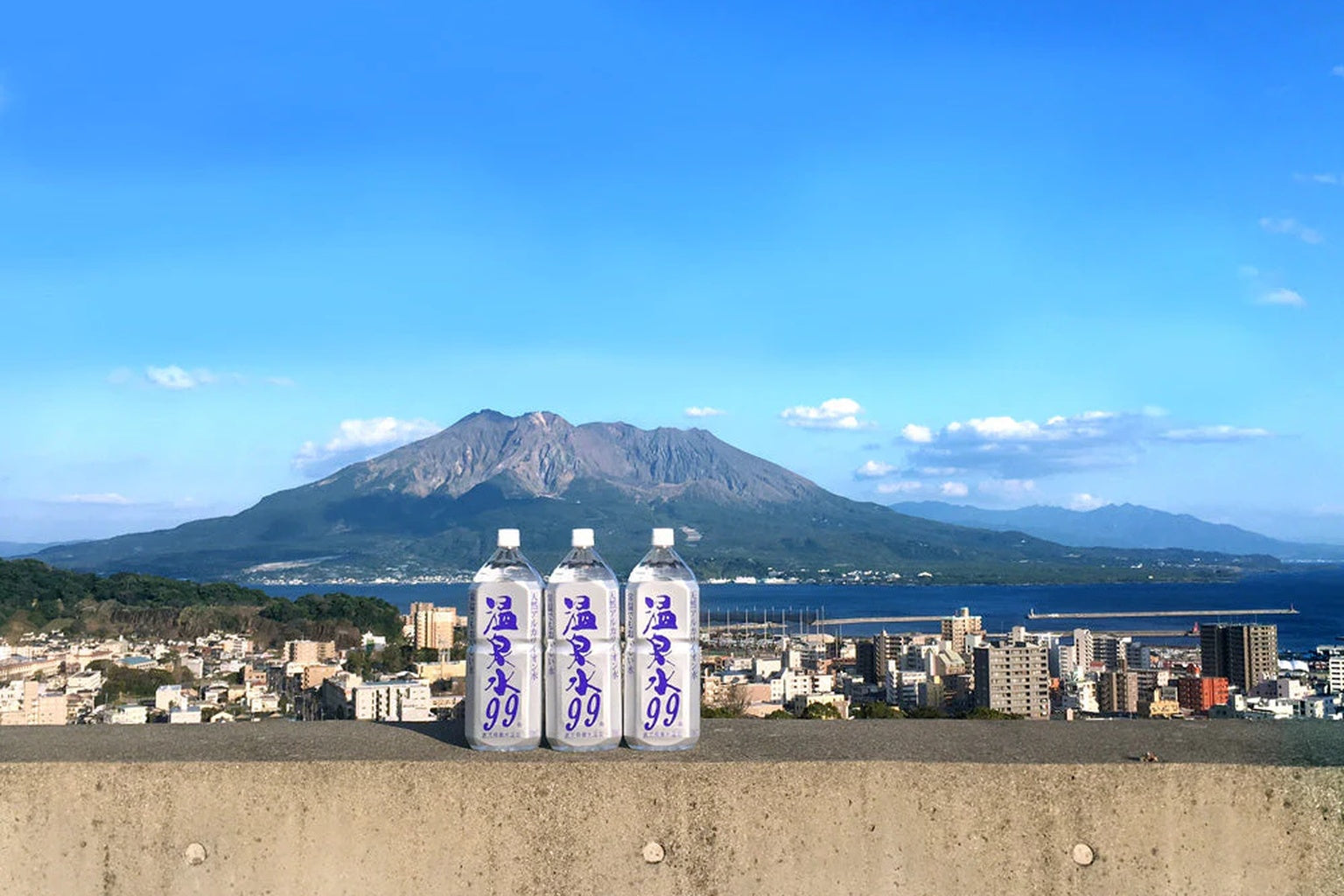 桜島を背景に並ぶ温泉水99のボトル｜鹿児島発ナチュラルウォーター