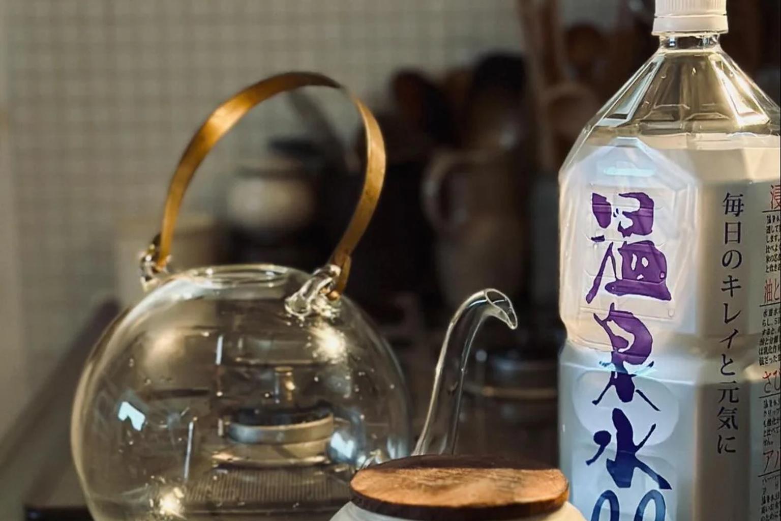 A serene kitchen scene featuring ONSENSUI 99 natural alkaline water beside a glass teapot under warm morning light.
