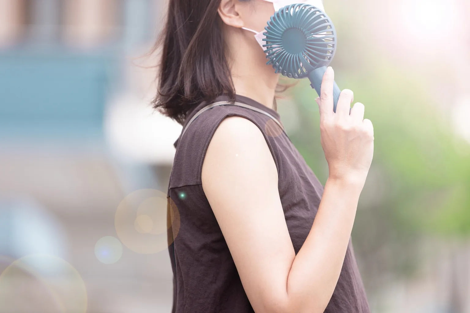 Woman using portable fan outdoors during hot summer day