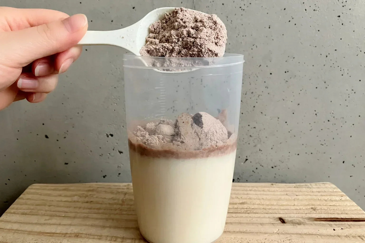 Protein powder being added to milk in a shaker, showing mixing protein with milk.