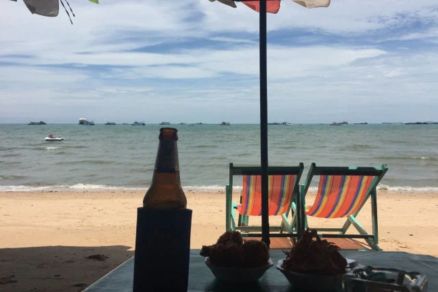 パタヤビーチの砂浜に並ぶデッキチェアとテーブル。南国の海を眺めながら過ごすリラックスタイム