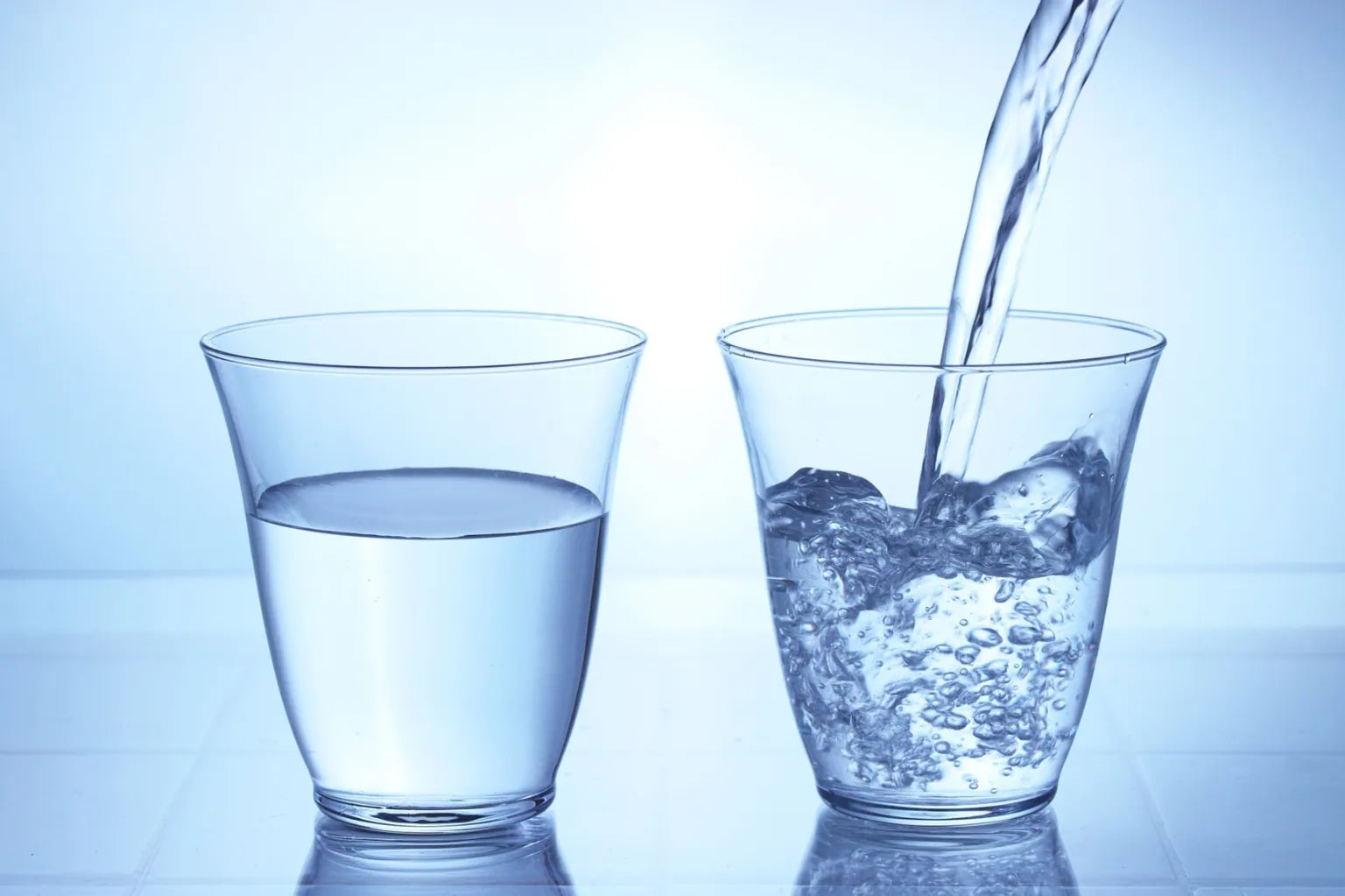 Two glasses of water being poured and compared, illustrating soft water clarity and purity inspired by Japanese ONSENSUI99.