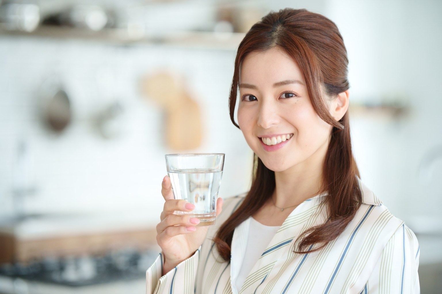 Smiling woman holding a glass of water in a bright kitchen
